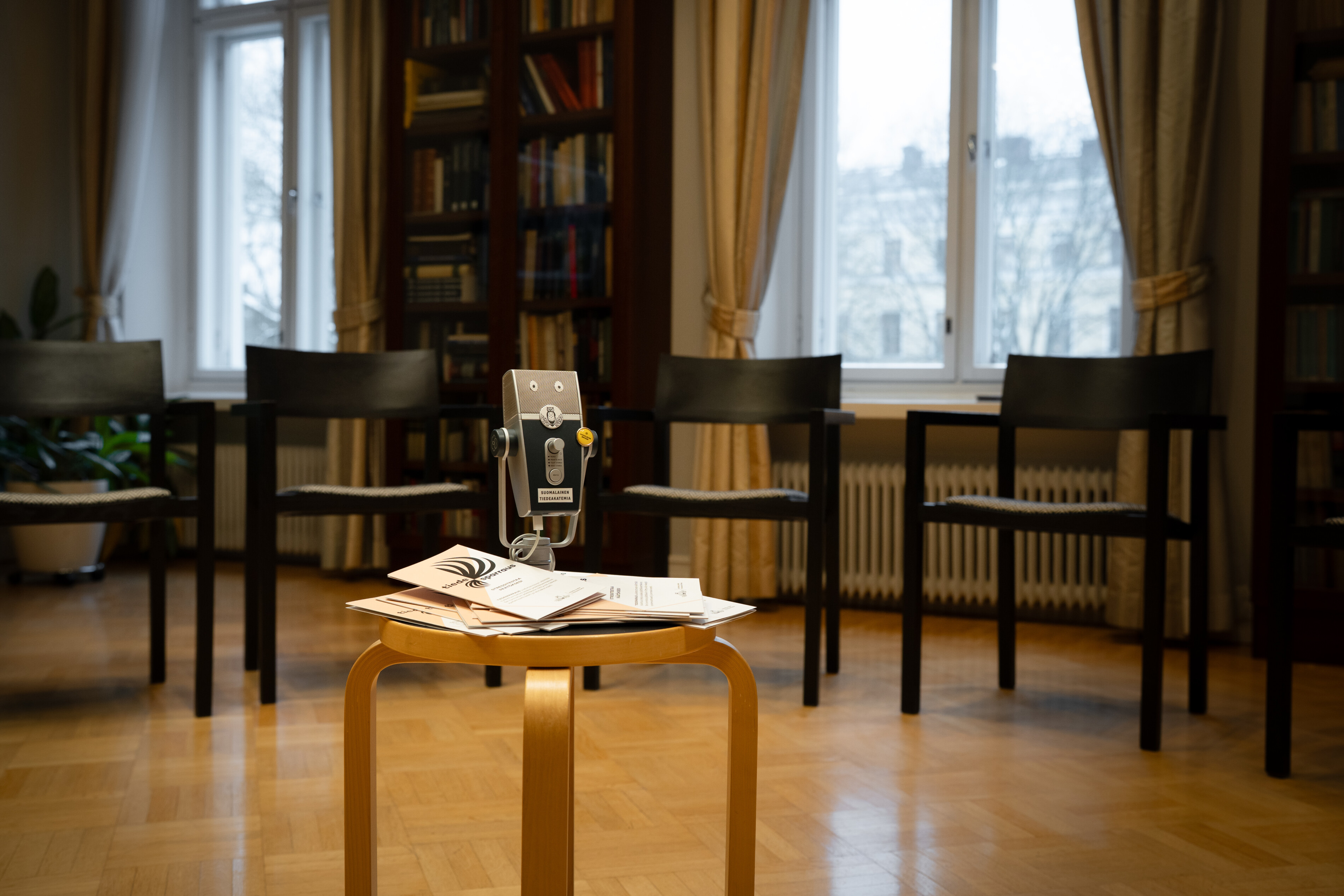 Tuolit on aseteltu huoneessa puolikaareen ja niiden keskellä on pöytä, jonka päällä on mikrofoni.